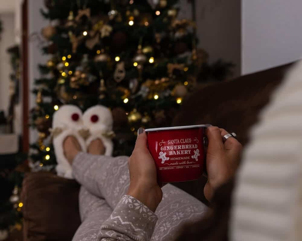 How to deal with family stress at Christmas - woman pictured holding a mug with feet up on sofa in front of Christmas tree.