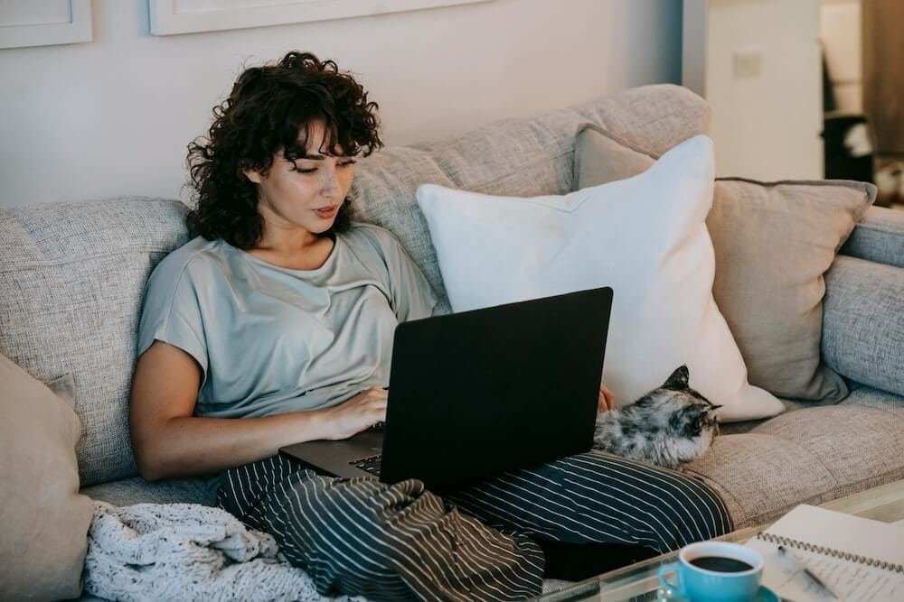 Woman on sofa with cat accessing online therapy on laptop